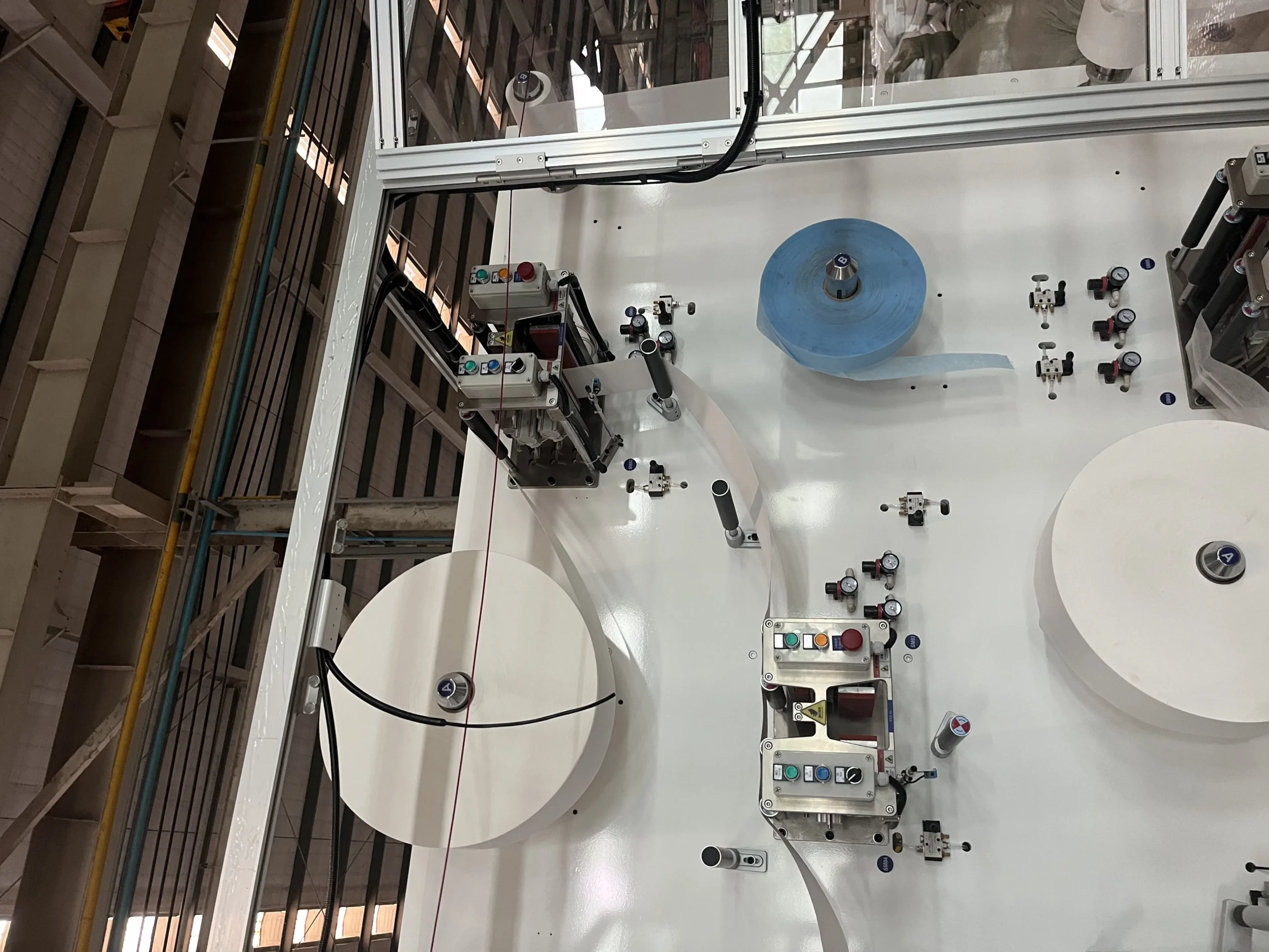 Multi-layer raw material unwinding zone on a Welldone disposable under-pad machine — non-woven topsheet and blue PE backsheet feeding simultaneously into the lamination station showing the 3-layer and 5-layer production architecture