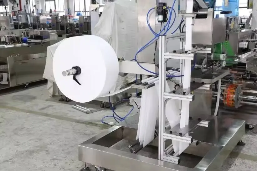 Non-woven master roll unwinding and web feeding into the folding tower on a Welldone wet wipes line — the Day 1 dry run station where web tension is re-established for a new substrate GSM before any lotion is introduced